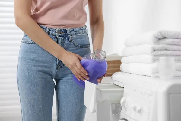 Woman pouring fabric softener into washing machine in bathroom, closeup