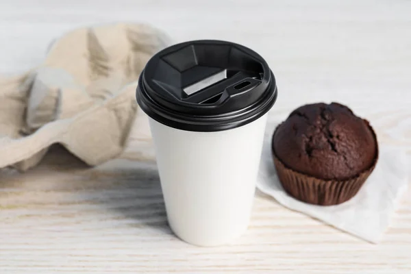 Paper cup with black lid and muffin on white wooden table, closeup. Coffee to go