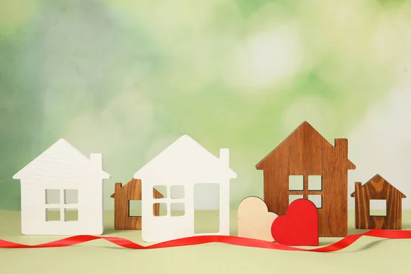 Long-distance relationship concept. House models, decorative hearts and red ribbon on light green background