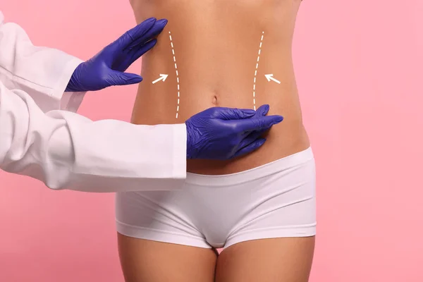 Doctor and patient preparing for cosmetic surgery, pink background. Woman with markings on her abdomen, closeup