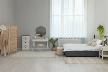 Şık bir yatak odası, geniş konforlu bir yatak ve pencerenin yanında bir şilte.