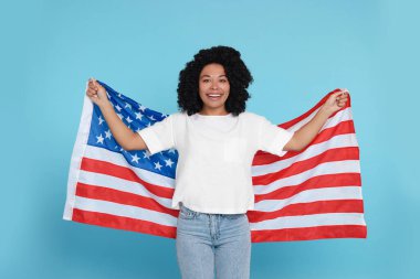 4 Temmuz - ABD 'nin Bağımsızlık Günü. Açık mavi arka planda Amerikan bayrağı taşıyan mutlu kadın.