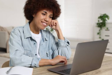 Odadaki ahşap masada dizüstü bilgisayar kullanan genç bir kadın.