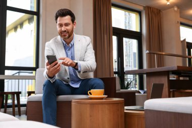 Kafede akıllı telefonunu kullanan yakışıklı bir adam.