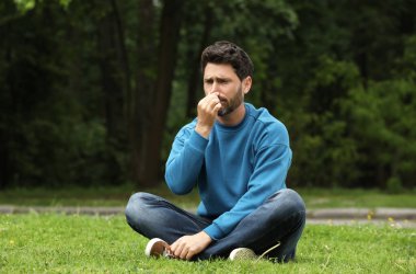 Parktaki yeşil çimlerde mevsimlik bahar alerjisi olan bir adam