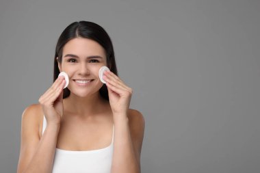 Gri arka planda pamuk pedlerle yüzünü temizleyen genç bir kadın. Metin için boşluk