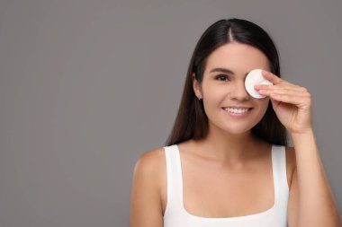 Gri arka planda pamukla yüzünü temizleyen genç bir kadın. Metin için boşluk