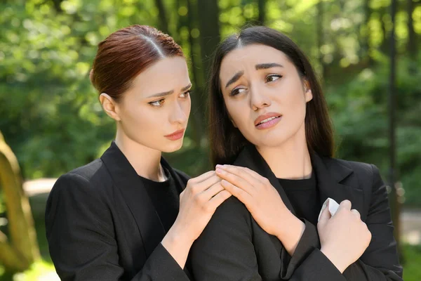 Sad women in black clothes mourning outdoors. Funeral ceremony