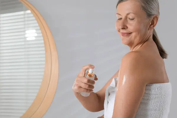 Happy woman applying body oil onto arm in bathroom. Space for text