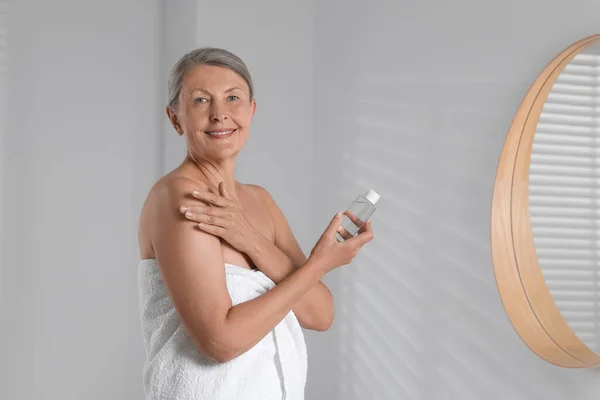 Happy woman holding bottle of body oil in bathroom. Space for text