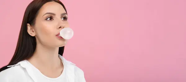 Beautiful woman blowing bubble gum on pink background, space for text