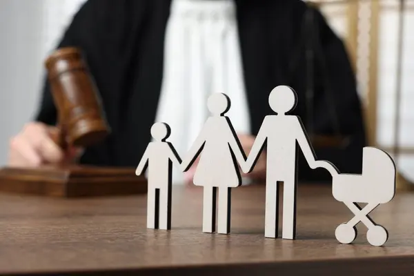 Family law. Judge with gavel sitting at wooden table, focus on figure of parents and children