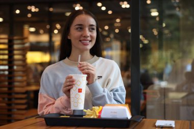 Lviv, Ukrayna - 26 Eylül 2023: Restorandaki masada McDonald 's içkisi, burgeri ve patates kızartması olan kadın