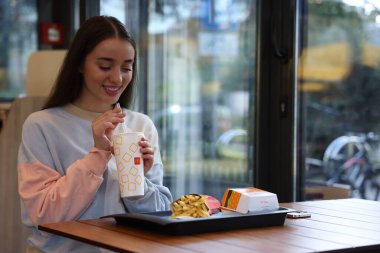 Lviv, Ukrayna - 26 Eylül 2023: McDonald 's' lı kadın restorandaki masada içki, burger ve patates kızartması, mesaj atmak için yer