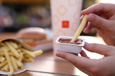 Lviv, Ukrayna - 26 Eylül 2023: McDonald 's' ın patates kızartmasını ahşap masada sosa batıran kadın, yakın plan