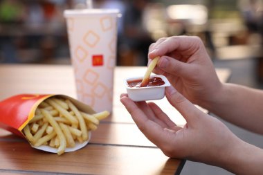 Lviv, Ukrayna - 26 Eylül 2023: McDonald 's' ın patates kızartmasını ahşap masada sosa batıran kadın, yakın plan