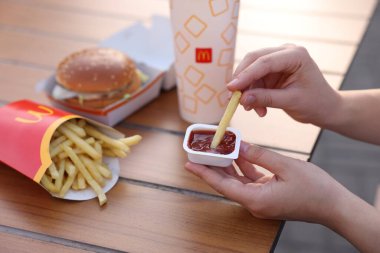 Lviv, Ukrayna - 26 Eylül 2023: McDonald 's' ın patates kızartmasını ahşap masada sosa batıran kadın, yakın plan