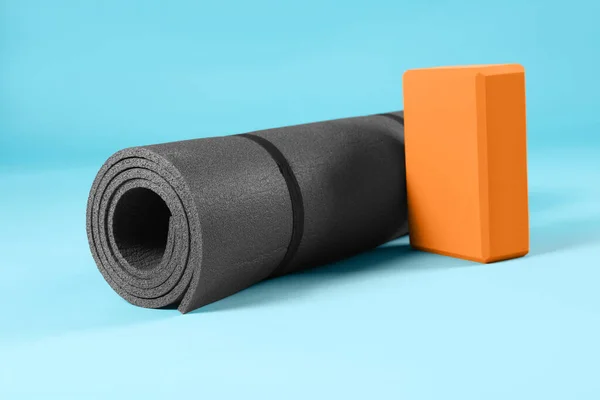 Exercise mat and yoga block on light blue background