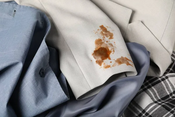 Dirty shirts and jacket with stain of coffee as background, closeup
