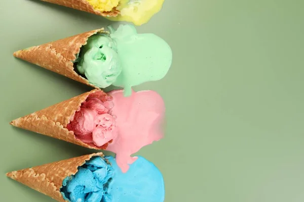 Melted ice cream in wafer cones on pale green background, flat lay. Space for text