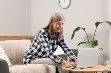 Evde dizüstü bilgisayar kullanan güzel bir yaşlı kadın.