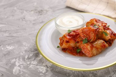 Domates sosu ve ekşi kremayla pişirilmiş lezzetli lahana dürümleri. Gri desenli masada, yakın plan. Metin için boşluk