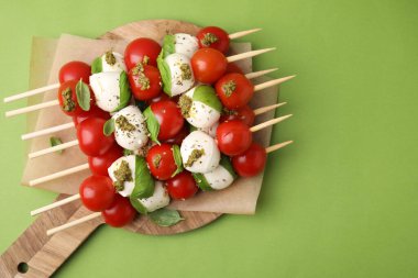 Yeşil arka planda domatesli şişler, mozarella topları fesleğen ve pesto sosu, üst manzara. Metin için boşluk