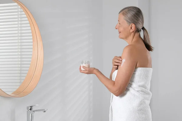 Happy woman applying body cream onto arm indoors. Space for text