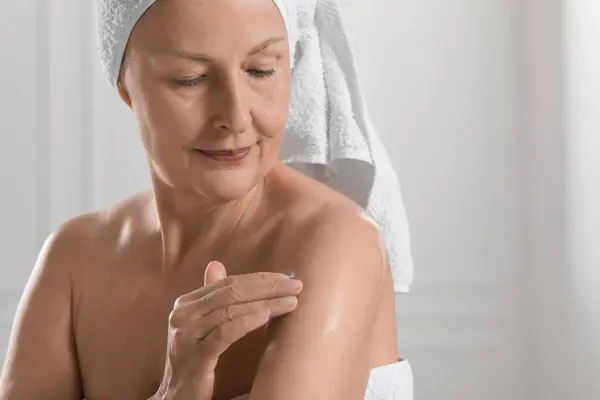 Happy woman applying body oil onto shoulder indoors. Space for text