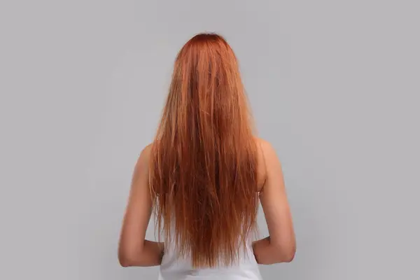 Woman with damaged messy hair on light grey background, back view