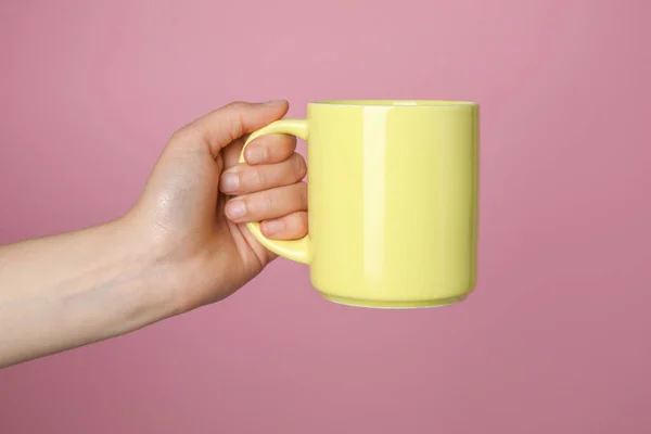 Woman holding yellow mug on pink background, closeup