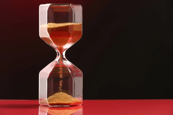 Hourglass with flowing sand on table against dark background. Space for text