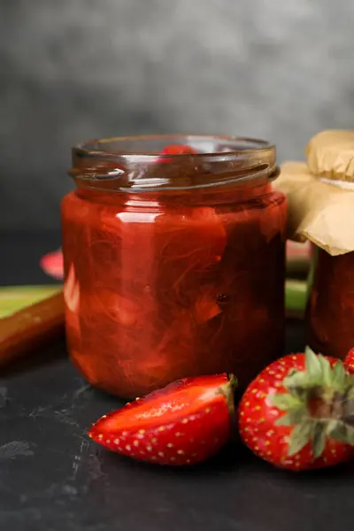 Jar of tasty rhubarb jam and strawberries on dark textured table