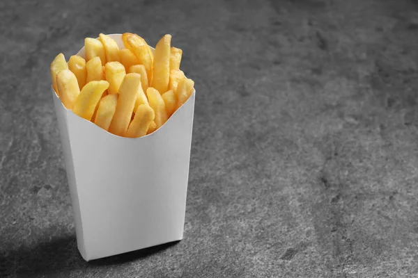 Delicious french fries in paper box on grey table, space for text