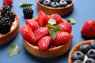 Tartlets with different fresh berries and mint on blue wooden table, closeup. Delicious dessert clipart