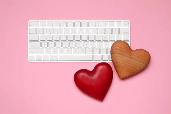 Long-distance relationship concept. Decorative hearts and keyboard on pink background, flat lay