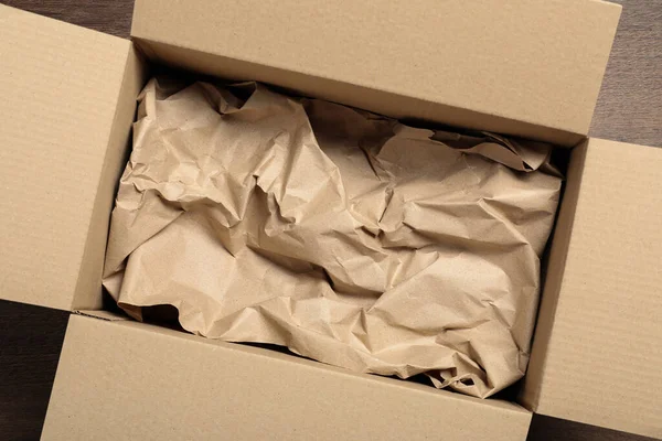 stock image Open cardboard box with crumpled paper on wooden floor, top view. Packaging goods