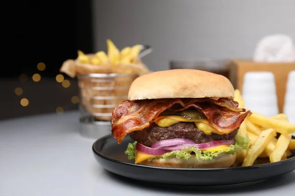 Tasty burger with bacon, vegetables and patty served with french fries on light grey table, closeup. Space for text