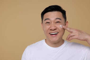 Açık kahverengi arka planda yüzüne krem süren yakışıklı bir adam. Metin için boşluk