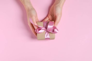 Elinde pembe arka planda fiyonklu hediye kutusu olan bir adam var.