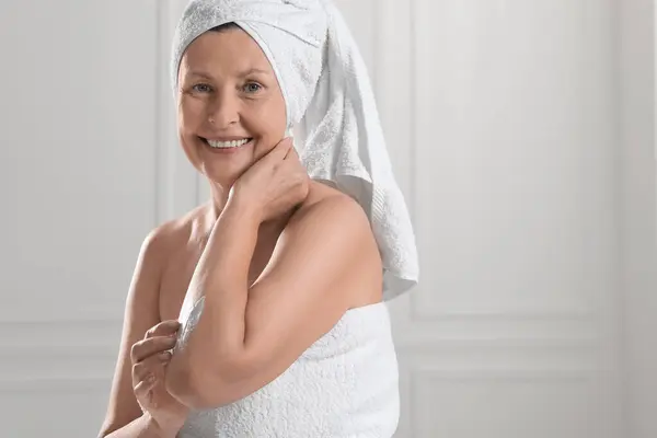 Happy woman applying body cream onto arm near white wall. Space for text