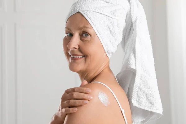 Happy woman applying body cream onto shoulder near white wall