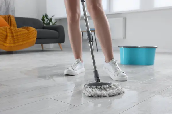 Woman cleaning floor with mop indoors, closeup