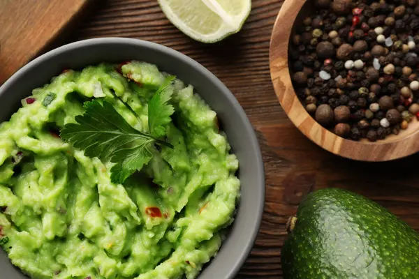 Lezzetli guacamole ve malzemeler ahşap masada, düz yerde.