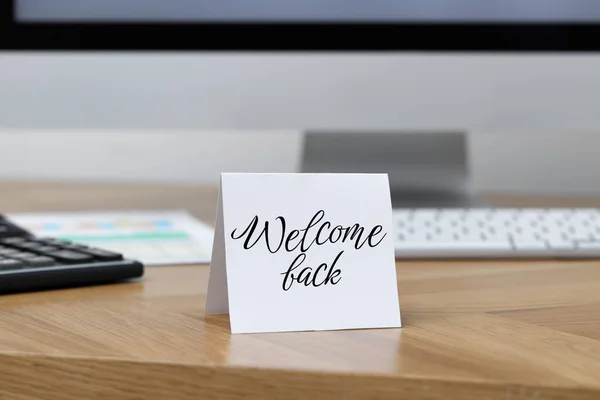 Paper note with phrase Welcome Back on office desk
