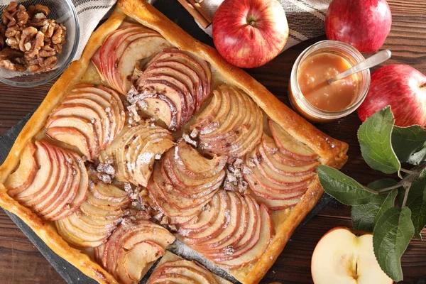Freshly baked apple pie and ingredients on wooden table, flat lay