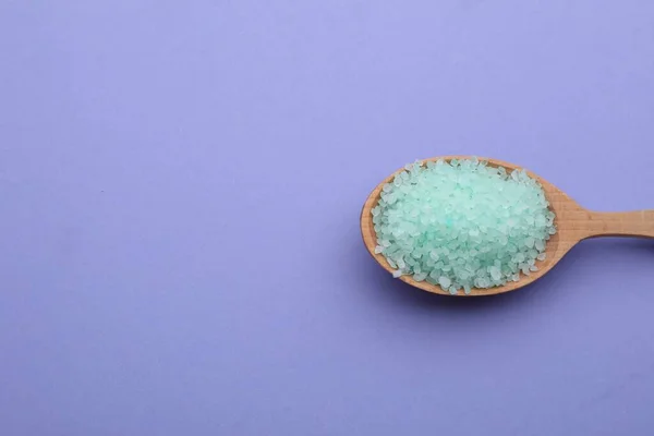 Spoon with turquoise sea salt on violet background, top view. Space for text