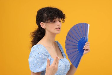 Elinde yelpaze olan kadın turuncu arka planda ısıdan muzdarip.