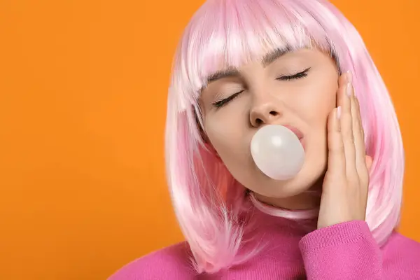Beautiful woman blowing bubble gum on orange background, space for text