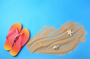 Parmak arası terlikler ve açık mavi arka planda kum. Metin için yeri olan düz bir yer. Plaj aksesuarları
